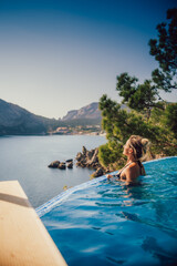 Beautiful girl on the edge of the pool, behind a beautiful spectacular view of the sea and mountains