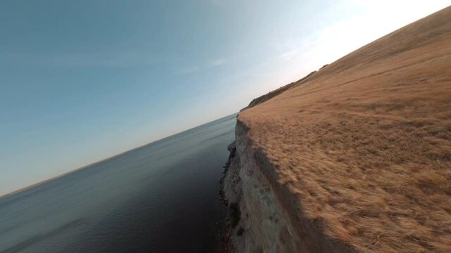 Sharp cliff on Volga river bank from cinematic fpv drone. Aerial shooting from flying drone over empty field on top cliff edge, wild lake and skyline background.