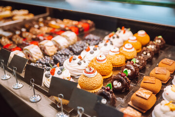 Different types of small cakes in candy store behind glass display