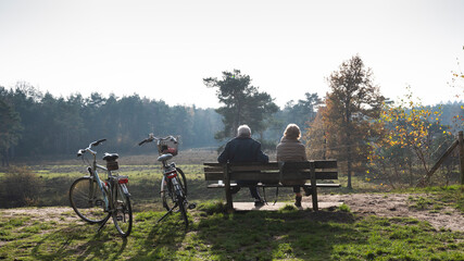 couple on bench resting from bicycle trip in autumn forest near Zeist in holland