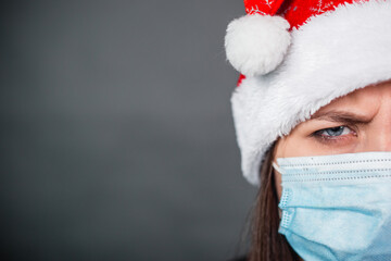 Close up portrait of woman in medical, disposable mask and Christmas red cap, half face in frame, copy space.