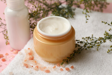 Fototapeta na wymiar Towel with jar of cosmetic cream on pink background 