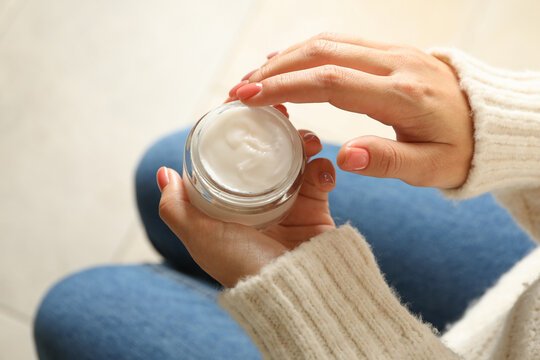Woman in sweater and jeans hold jar of cosmetic cream