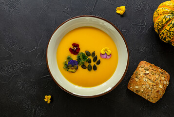 Vegan pumpkin cream soup with edible flowers, seeds and bread