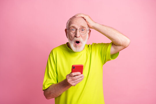 Photo of old shocked surprised man wear lime t-shirt hold hand head use smartphone isolated on pink color background