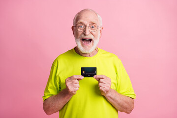 Photo of old happy excited cheerful grandfather wear lime t-shirt hold credit card isolated on pink color background