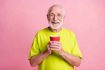 Portrait of funky optimistic pensioner hold cup wear spectacles lime color t-shirt isolated on pastel pink color background
