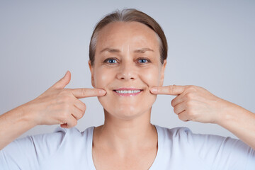 Portrait of a mature woman in a white T-shirt, touching her face with her fingers, looking at the camera. Anti-wrinkle facial skin care concept.