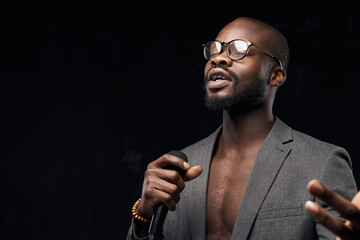 portrait of a dark-skinned handsome guy in grey jacket and glasses  on a black background, singing in a microphone  with closed eyes