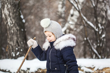 Girl child walking in the winter forest in a blue jacket and gray hat, snow and snowflakes, frosty air, baby's smile