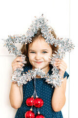 Baby girl in blue dress holding new year's Christmas decoration star, bright interior and waiting for the holiday