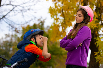 Brother and sister are arguing between riding bicycles who is stronger, the boy shows his strength. They rest, smile and look at each other. Photo from the autumn park.