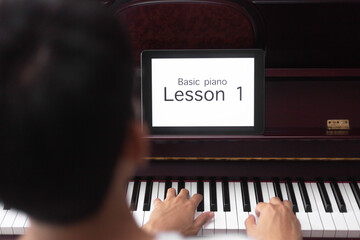 young Asian man learning basic of classic piano online by tablet at home.
