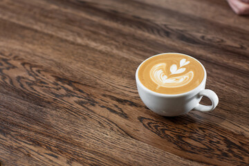 White cup of hot latte coffee with beautiful milk foam latte art texture isolated on wooden background. Overhead view, copy space. Advertising for cafe menu. Coffee shop menu.