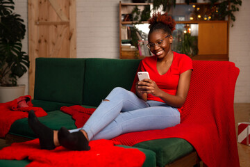 Obraz premium beautiful young african female sitting with mobile phone on the sofa