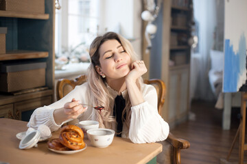 A young woman has breakfast with tea and pastries with jam.