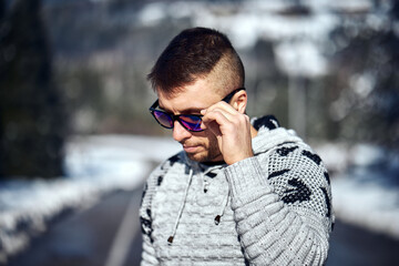 Young confident bearded man brutally posing in a winter forest in sunglasses and a knitted sweater