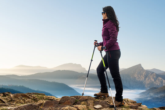 Female hiker with walking poles looking at mountains.