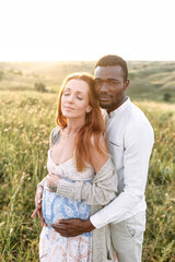 Handsome african american man is hugging his charming pregnant wife on the summer meadow