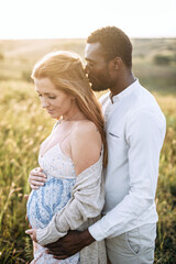 Handsome african american man is hugging his charming pregnant wife on the summer meadow