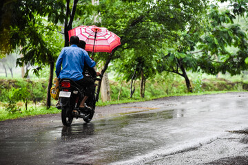 Obraz premium Men riding a bike in rainy day holding an umbrella