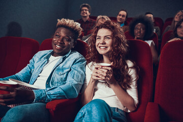 A man with a woman sits in a cinema and smiles.