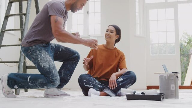 Man brings woman coffee as couple sit on floor wearing old clothes with paint chart ready to decorate new home - shot in slow motion