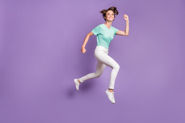 Fototapeta na wymiar Full size profile photo of sweet pretty girl jumping hands fists wear white sneakers trousers blue t-shirt isolated on violet background