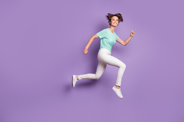 Fototapeta na wymiar Full size profile photo of sweet optimistic girl jumping hands fists wear white sneakers trousers blue t-shirt isolated on violet background