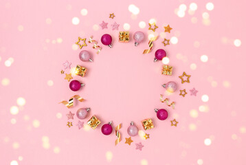 Wreath made of Christmas decorations and gold confetti. Minimalist festive frame on a pink pastel background.