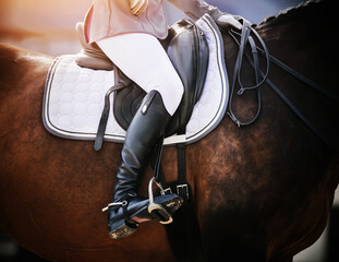 On a Bay sports horse in a leather saddle sits a rider in black boots with spurs, holding the reins...