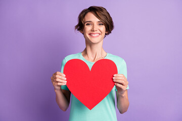 Photo of lovely young woman dressed casual turquoise clothes holding big red heart isolated violet color background