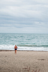 A woman going into the cold sea with her bathing suit on November 9-th 2020. Autumn winter season on the beach.