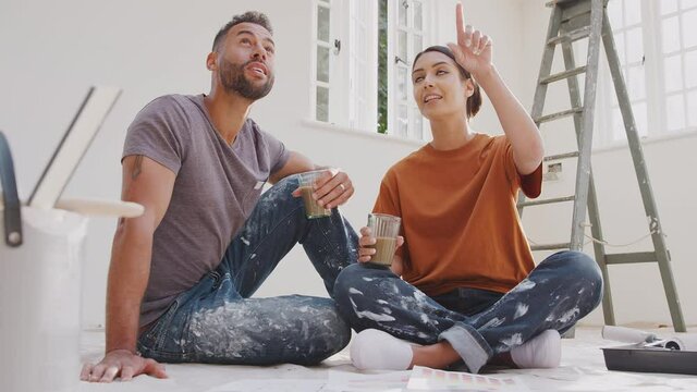 Couple sitting on floor drinking coffee wearing old clothes with paint chart ready to decorate new home - shot in slow motion