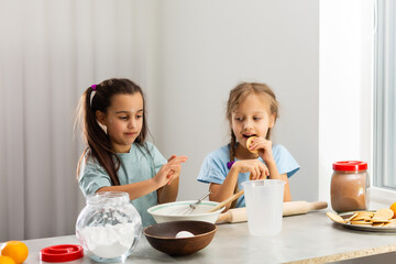 Two little girls in the kitchen prepare food, a dessert for the family. As they learn to cook they start playing with flour and smiling each other. Concept of: cooking classes, family, education.