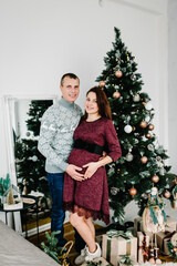 Pregnant couple in love near Christmas tree. Happy New Year and Merry Christmas. Christmas decorated interior. Pregnancy, family holidays, people and expectation concept.