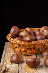 Top view of chestnuts in basket on rustic wooden table, with selective focus, black background, horizontal, with copy space