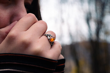 Young woman blowing warm air into hands in forest during autumn with shinny ring on finger.