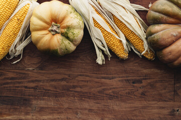 Corn cob and pumpkin on brown wooden board