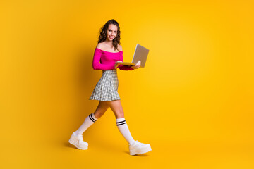 Full length body size photo of busy female teenager keeping laptop smiling typing communicating going fast isolated on bright yellow color background