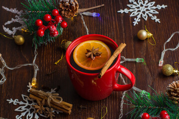 Delicious warm mulled wine with cinnamon, star anise and orange in a red cup on a Christmas background.