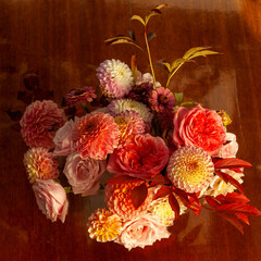 Floral composition of dahlia flowers, roses and autumn leaves. Arty, bright red and pink color  bouquet of flowers on wooden table 