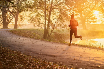 Athletic man running in the park during fall autumn morning