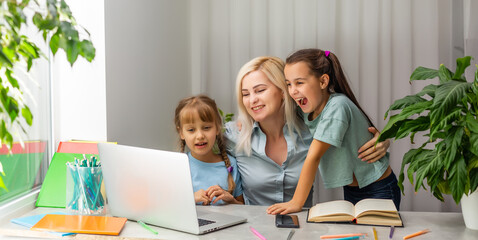 happy mother works at a laptop and two little daughters play