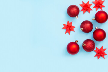 Red Christmas balls and paper stars on a pastel blue background. Minimal festive composition. Copy space for text.
