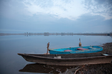 Obraz premium Foggy sunrise over the lake. Lonely boats on the shore.