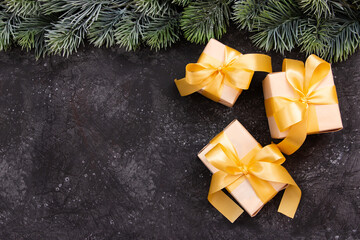 Fototapeta na wymiar Beautiful Christmas gifts with a gold bow and a fir branch on a dark black background. Flat design. Copy space.