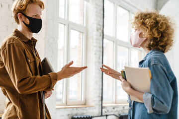 Young pleased friends in face masks talking and looking each other