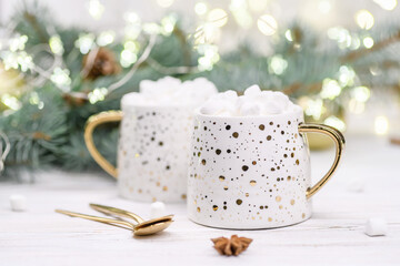Fototapeta na wymiar White cup of cappuccino or cocoa with christmas tree on the buckground of gold bokeh, New Year hot drink