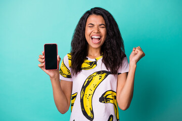 Photo of pretty excited lady hold telephone screen empty space closed eyes wear banana print t-shirt isolated teal color background